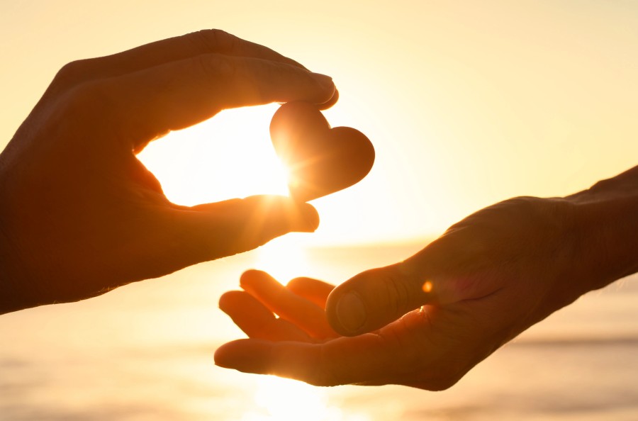 Hands forming a heart shape at sunset, symbolizing charitable giving